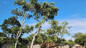 A row of wooden cabins with a central garage-style building, surrounded by trees and a clear sky. - Carmel River Inn & Cottages (Carmel)