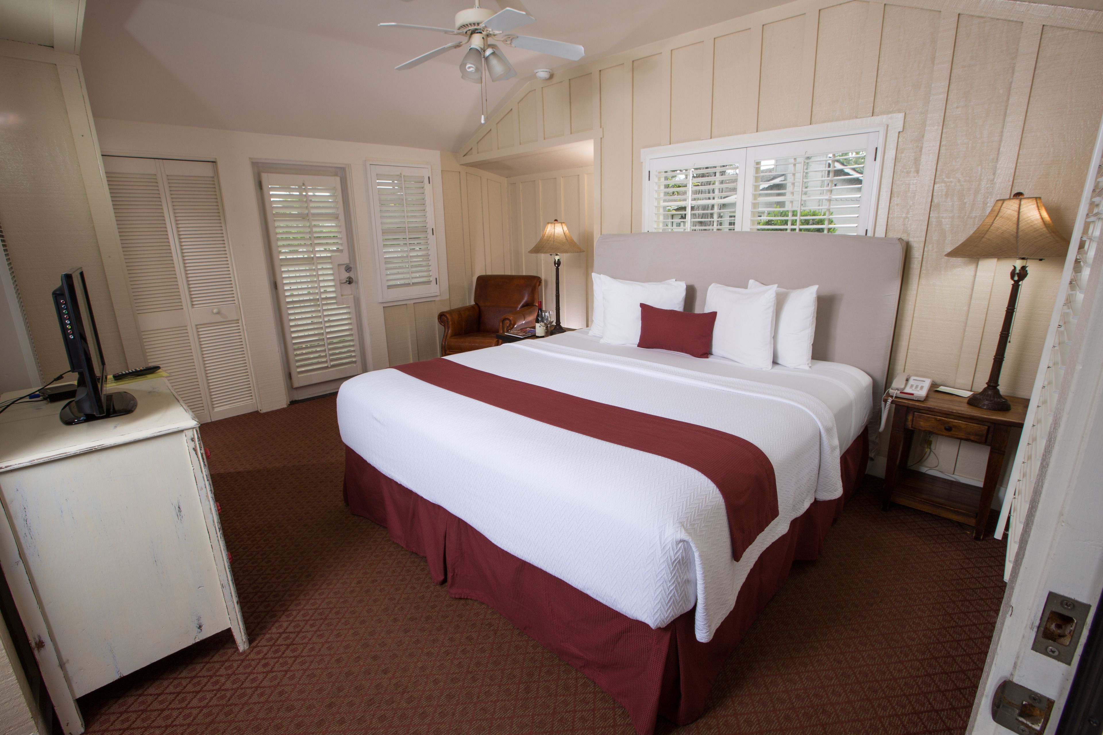 A hotel room with a large bed, two bedside lamps, a ceiling fan, and a desk with a computer.