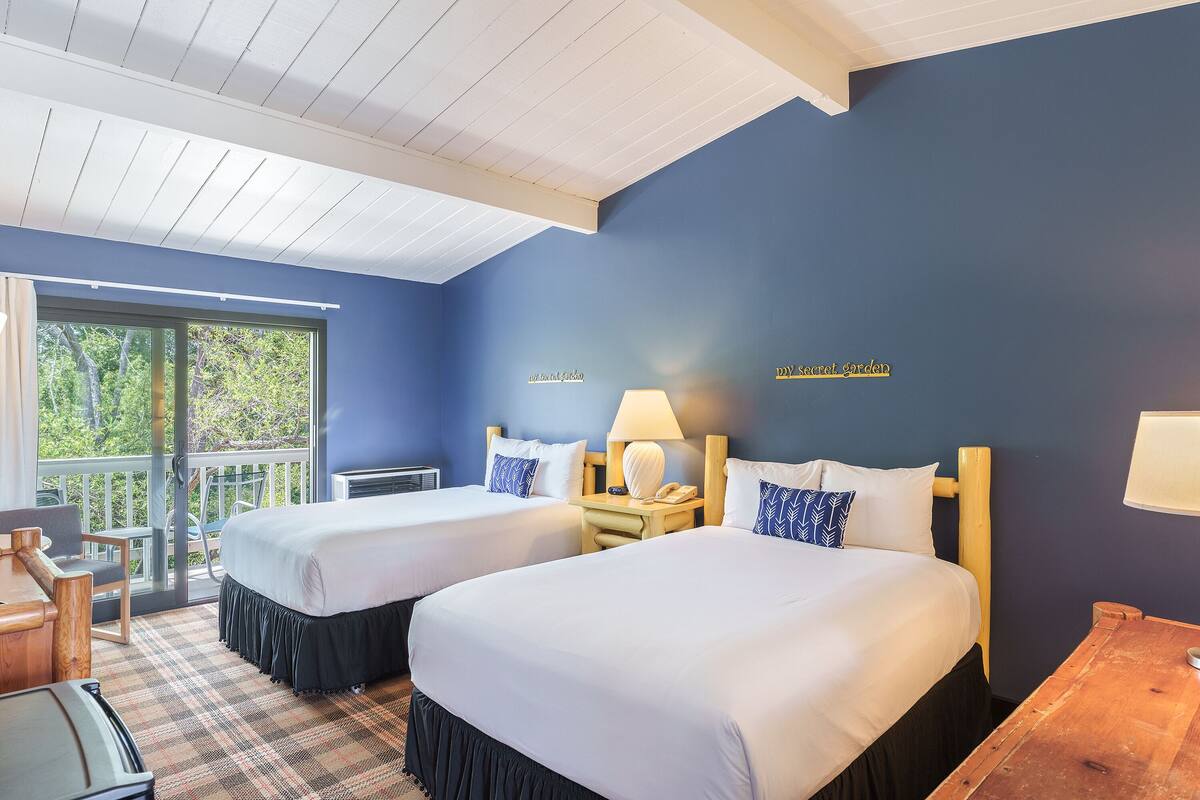 Ein Hotelzimmer mit zwei Betten, einem Holztisch, einem Stuhl, einem Tisch und Blick ins Freie.