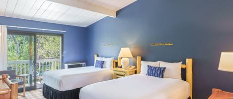 Une chambre d’hôtel avec deux lits, un bureau en bois, une chaise, une table et une vue sur l’extérieur.