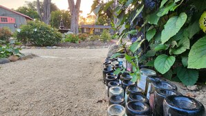 A garden with a gravel path, a row of empty glass jars, and a house in the background. - Carmel River Inn & Cottages (Carmel)
