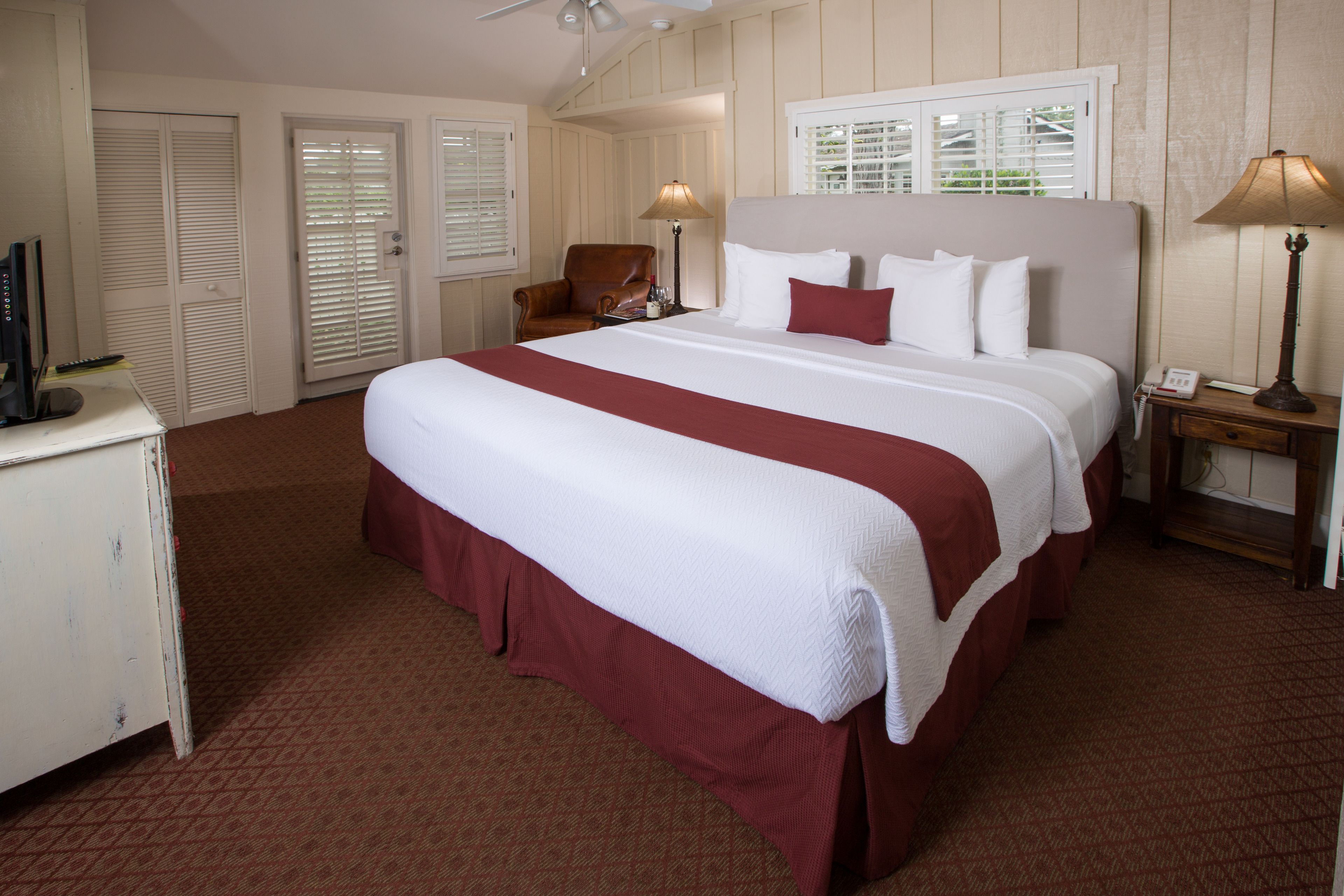 A hotel room with a large bed, a desk, a chair, and a window with blinds.