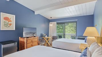 A hotel room with two beds, a TV, a wooden dresser, a small table, and a balcony with a view of greenery.