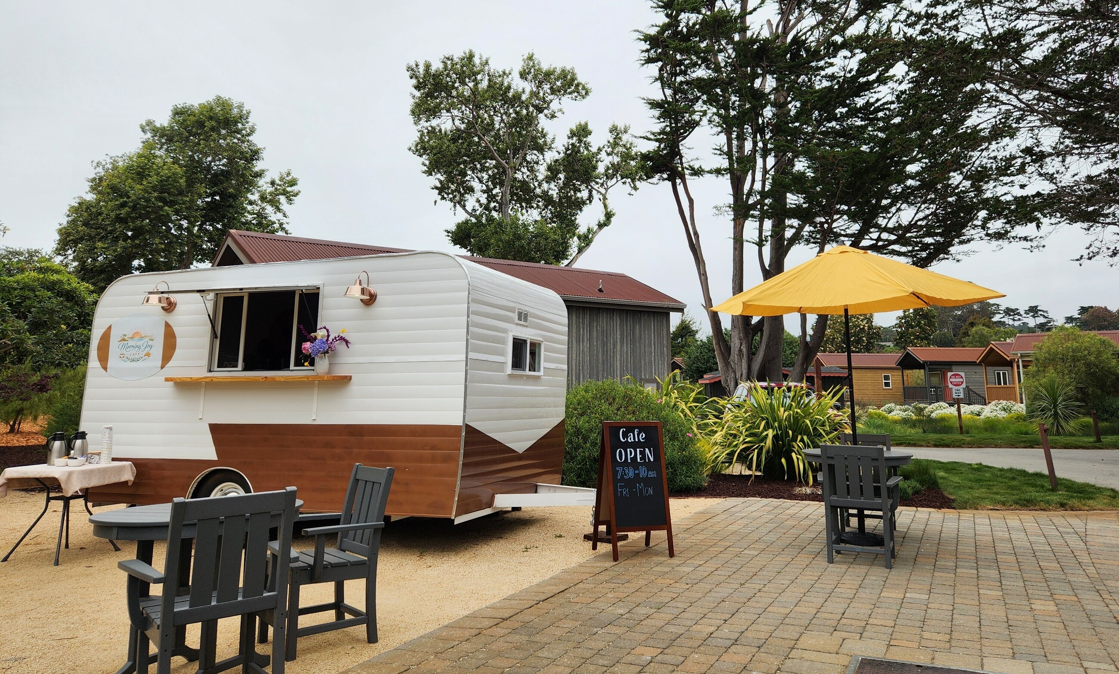 A mobile cafe with a small seating area, a table with chairs, and a yellow umbrella.