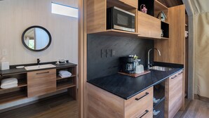 A modern bathroom with a wooden vanity, a sink, a mirror, and a built-in microwave. - Carmel River Inn & Cottages (Carmel)
