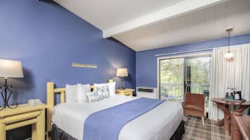 A hotel room with a large bed, two bedside tables with lamps, a wooden chair, a small table with a coffee maker, and a view of greenery through the window.