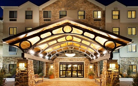 A hotel entrance with a stone facade, a covered patio area, and a large glass door.