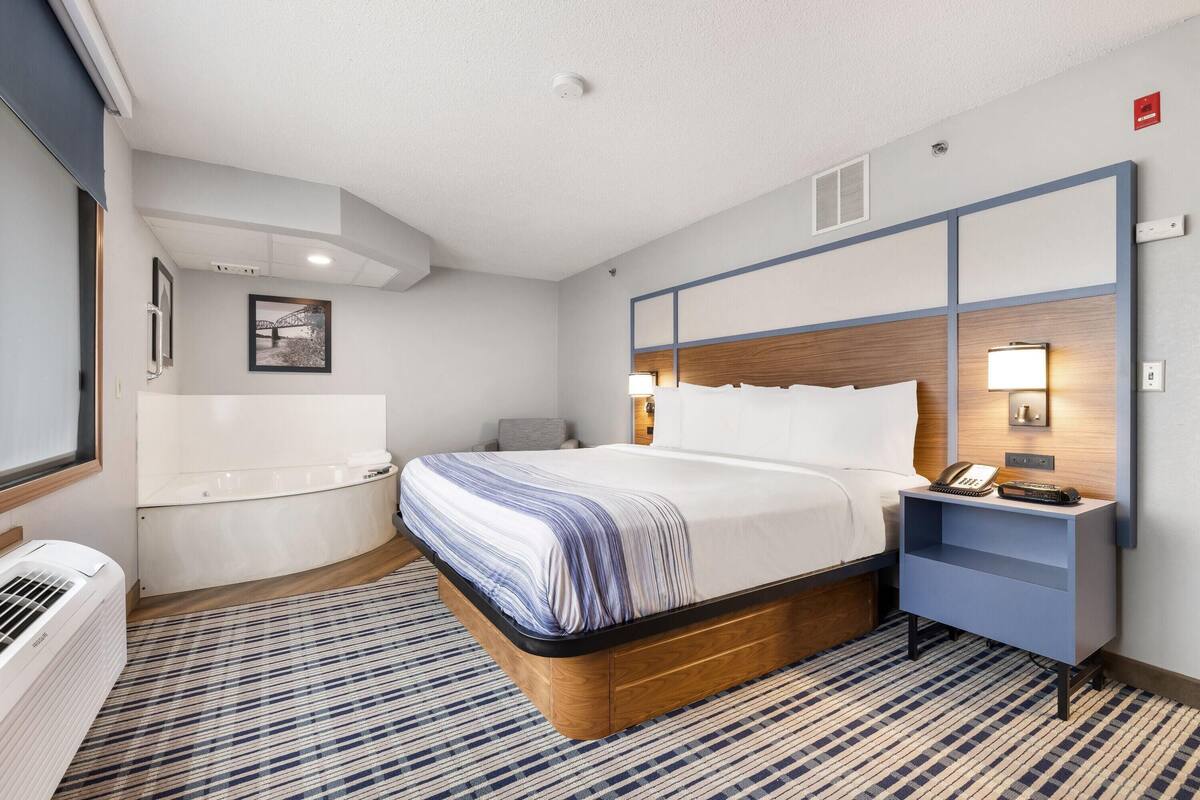 A hotel room with a bed, bedside table, and a wall-mounted heater.