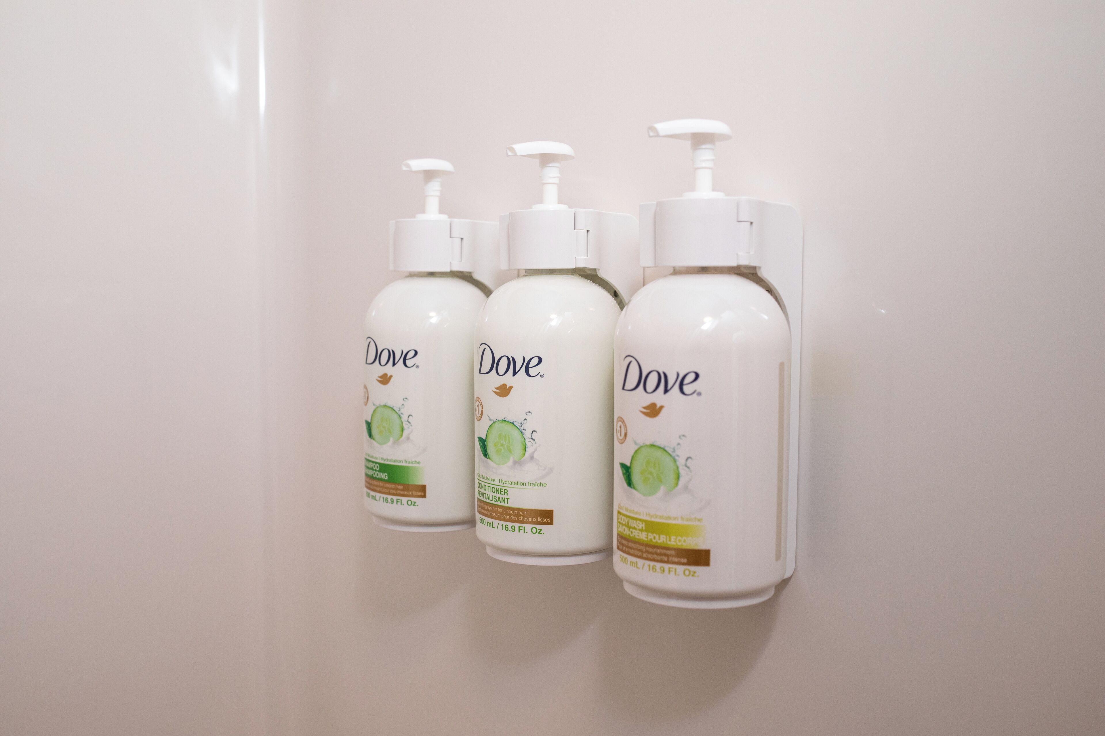 Tres botellas de jabón Dove frente a una pared lisa.