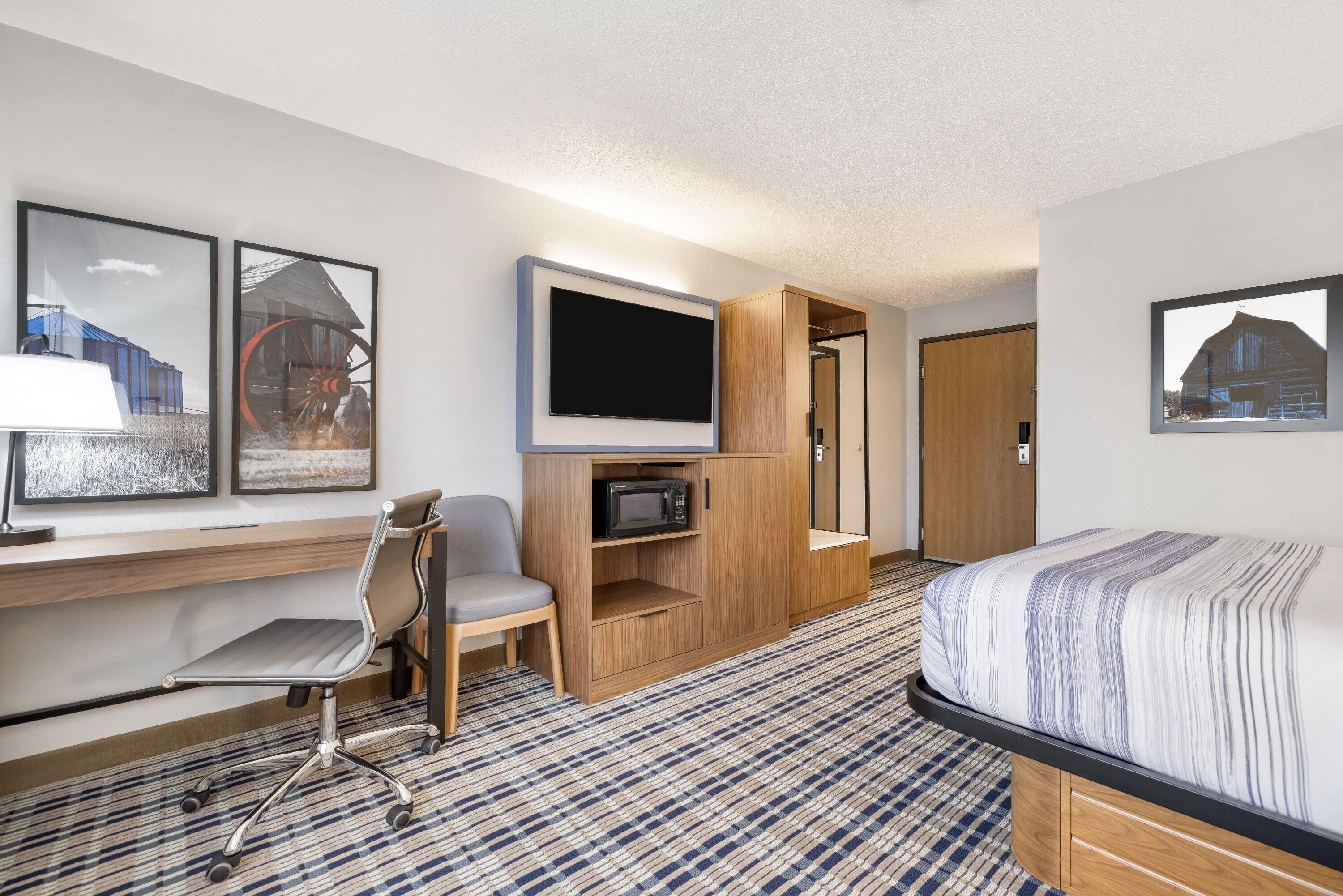 A hotel room with a bed, a desk with a computer, a chair, a TV, and a microwave.