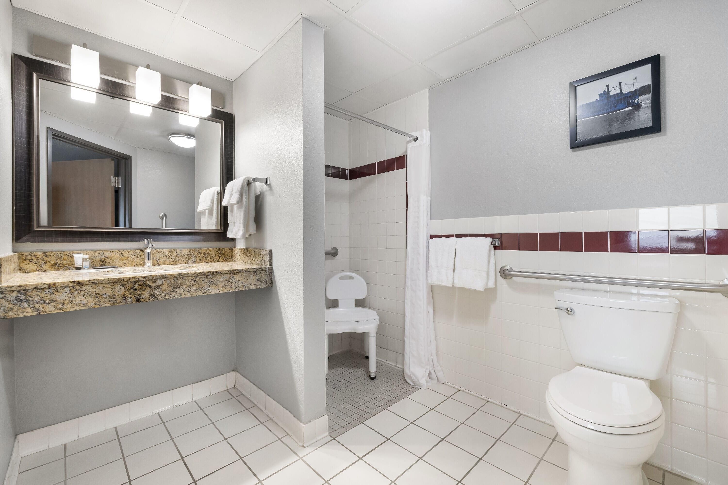 A bathroom with a large mirror, a sink, a toilet, and a shower area.