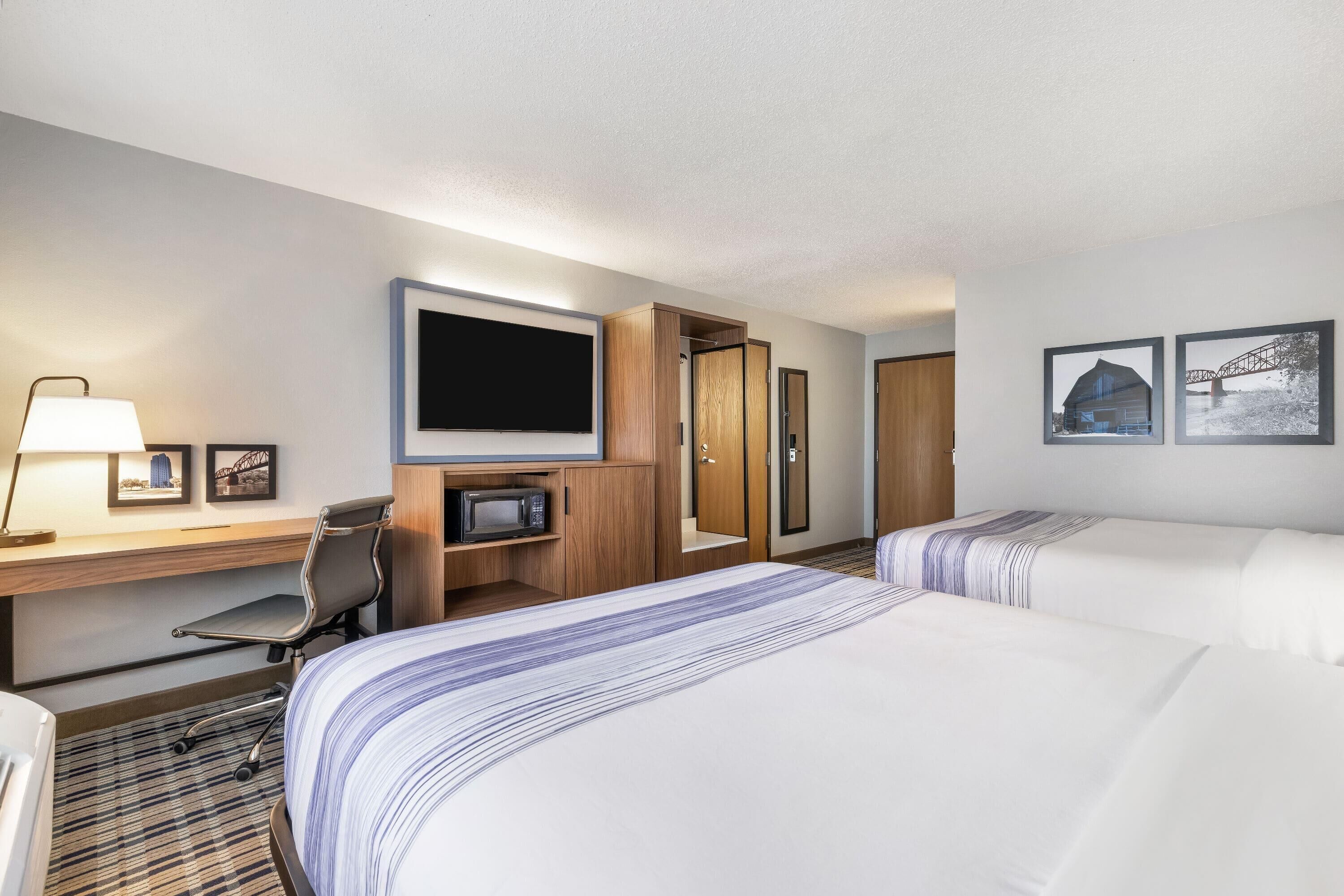 Une chambre d’hôtel avec deux lits, un bureau avec un ordinateur, une télévision et un four à micro-ondes.