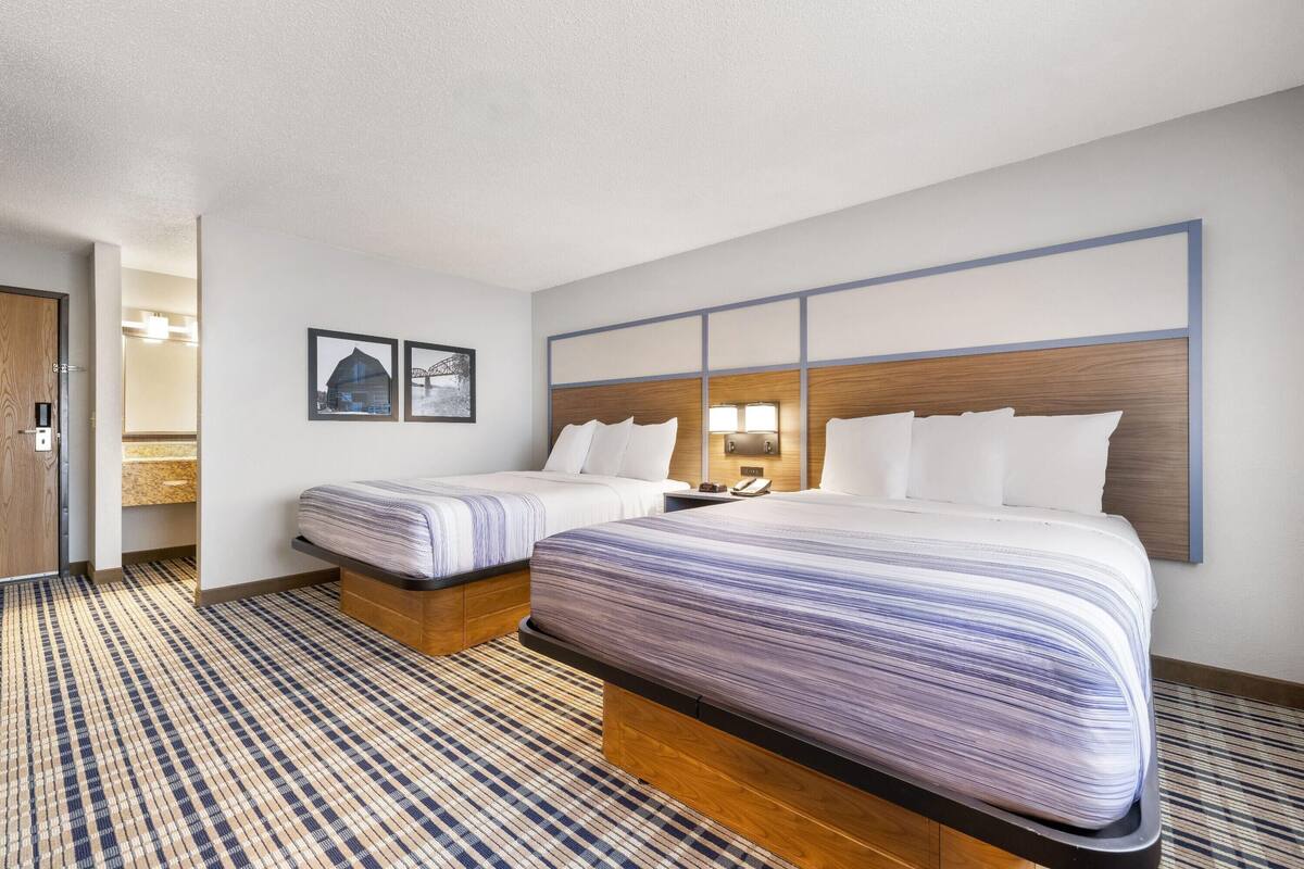 A hotel room with two beds, a wooden headboard, a wall-mounted phone, and a framed picture.