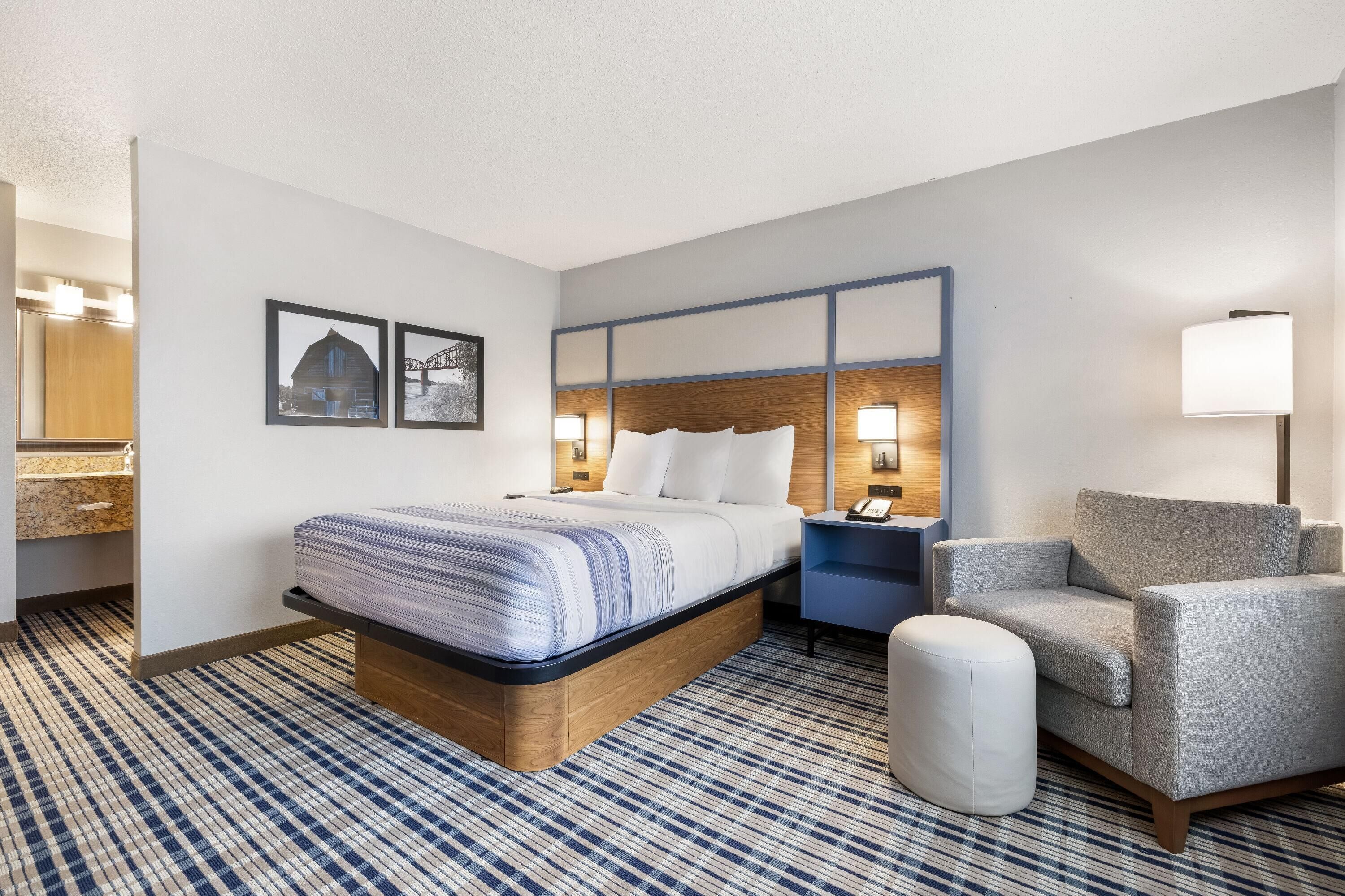 Une chambre d’hôtel avec un grand lit, une chaise, une table de chevet et une lampe fixée au mur.