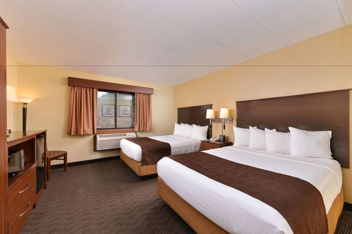 A hotel room with two beds, a desk, a chair, a lamp, and a window with curtains.