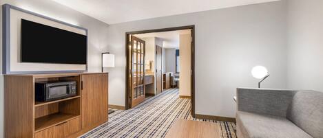 Habitación de hotel moderna con televisión de pantalla plana, microondas, sofá, mesa de centro y pasillo que conduce a un baño.