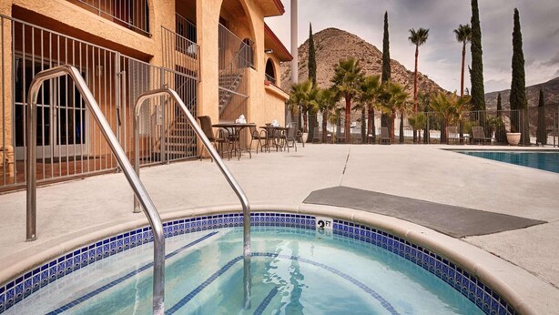 Ein Swimmingpool mit einer gefliesten Kante, einer Metallleiter und einer Terrassenanlage mit Tischen und Stühlen.