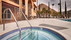 Una piscina con borde de azulejos, escalera metálica y zona de patio con mesas y sillas.