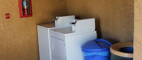 A laundry area with a washing machine, a blue trash bin, and a red fire extinguisher on the wall.