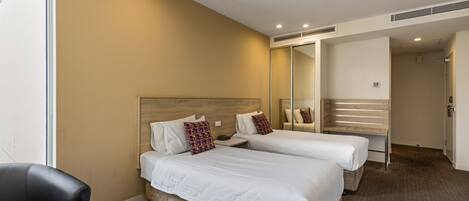 Habitación de hotel con dos camas, un espejo grande, una silla y una puerta visible que da a otra habitación.