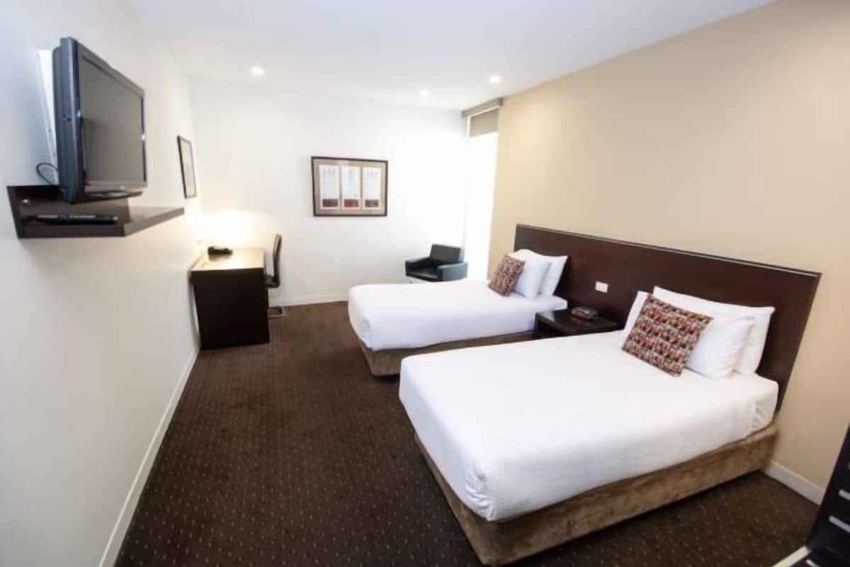 Quarto de hotel com duas camas, televisão, escrivaninha e mesa de cabeceira.
