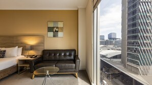 Una habitación de hotel moderna con sofá de cuero, una mesa de centro de vidrio, una cama y vistas a la ciudad.