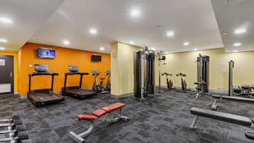 Un gimnasio con cintas de correr, elípticas, prensa de banca y pesas sueltas.
