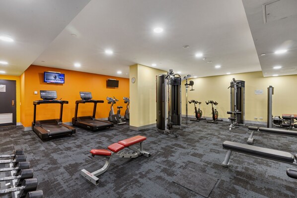A gym with treadmills, elliptical machines, a bench press, and free weights.