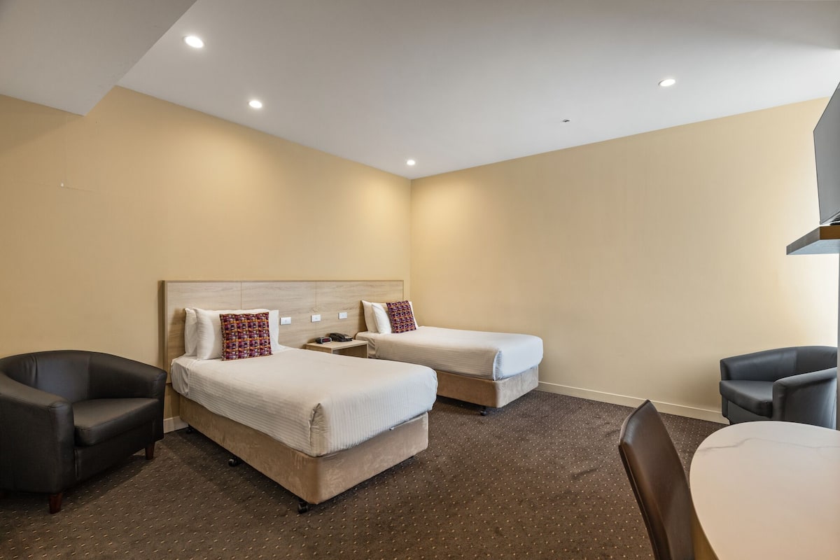 Quarto de hotel com duas camas, uma secretária, uma cadeira e uma mesa de jantar.