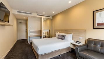 Ein Hotelzimmer mit einem großen Bett, einem Nachttisch mit Telefon, einem Ledersessel und einem Spiegel an der Wand.