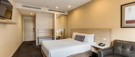 Una habitación de hotel con una cama grande, una mesita de noche con un teléfono, un sillón de cuero y un espejo en la pared.