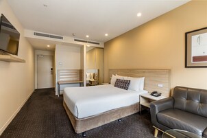 Una habitación de hotel con una cama grande, una mesita de noche con un teléfono, un sillón de cuero y un espejo en la pared.