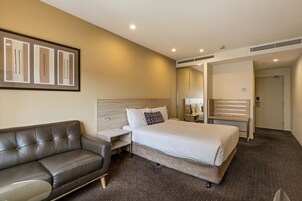 Una habitación de hotel con cama, sofá de cuero, mesita de noche, espejo y puerta.
