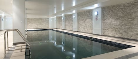 Una piscina interior moderna con agua cristalina, suelo de baldosas y una barrera de vidrio.