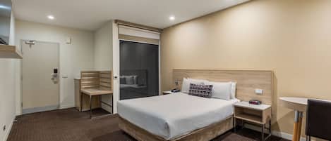 A hotel room with a large bed, a desk, a chair, a wardrobe, and a small table.