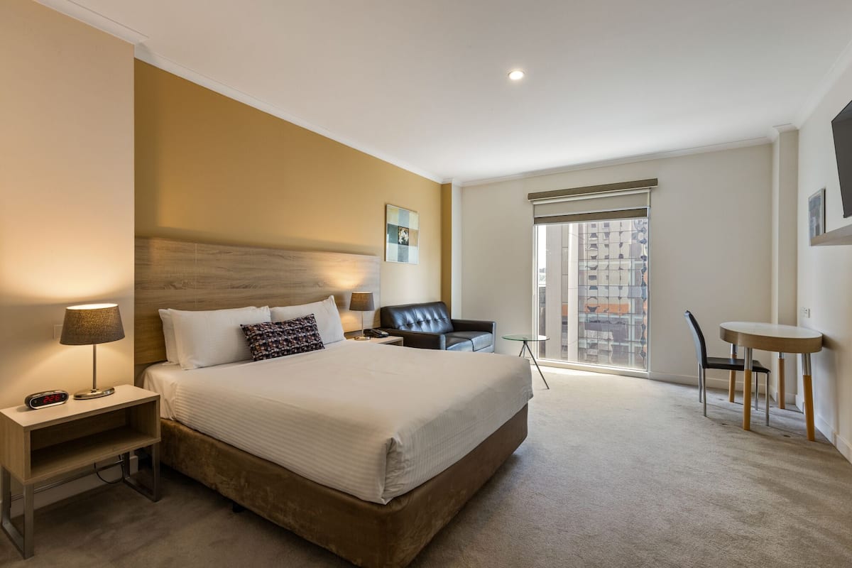 Quarto de hotel com uma cama grande, uma escrivaninha, uma cadeira e uma mesinha.