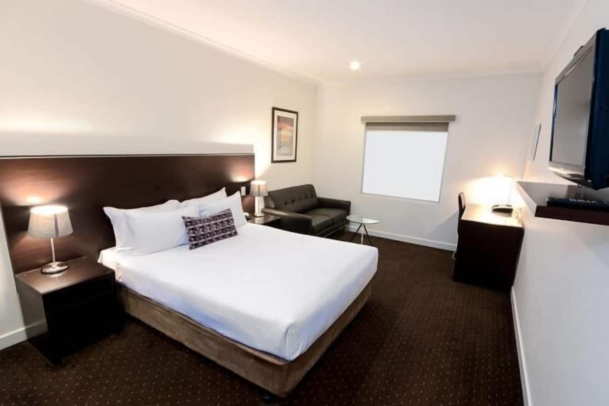 Quarto de hotel com cama, escrivaninha, cadeira, televisão e janela.