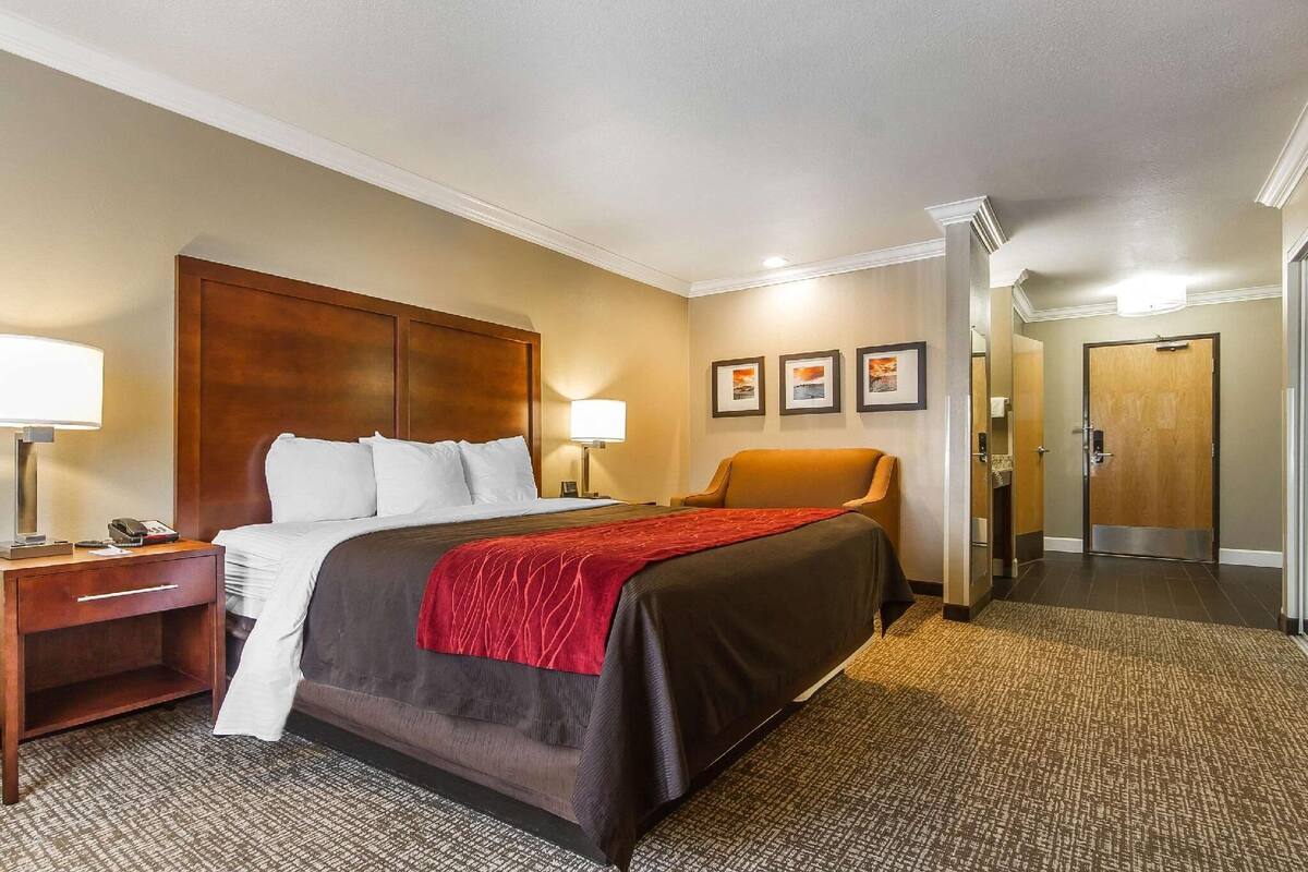 A hotel room with a bed, bedside tables, a chair, and a door leading to a hallway.