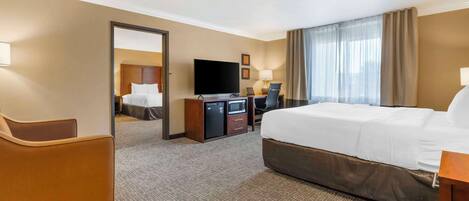 A hotel room with a large bed, a desk with a computer, a television, and a seating area with a chair.