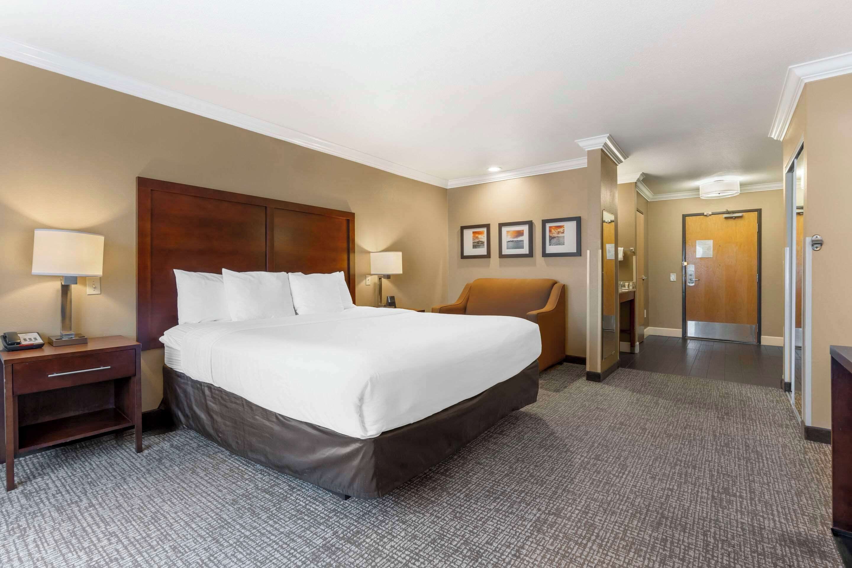 A hotel room with a large bed, a nightstand, a chair, and a door leading to the hallway.