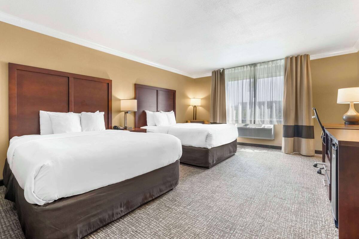 A hotel room with two beds, a desk, a lamp, and a window with curtains.