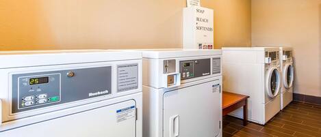 A laundry room with two front-loading machines and a sign indicating the location of soap, bleach, and softeners.