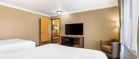 Habitación de hotel con dos camas, televisión, escritorio con ordenador, una silla y ventana con cortinas.