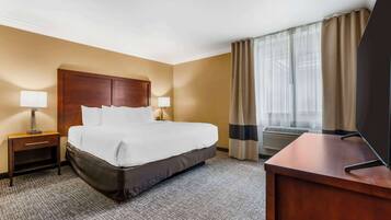 A hotel room with a large bed, two bedside tables with lamps, a desk, and a window with curtains.