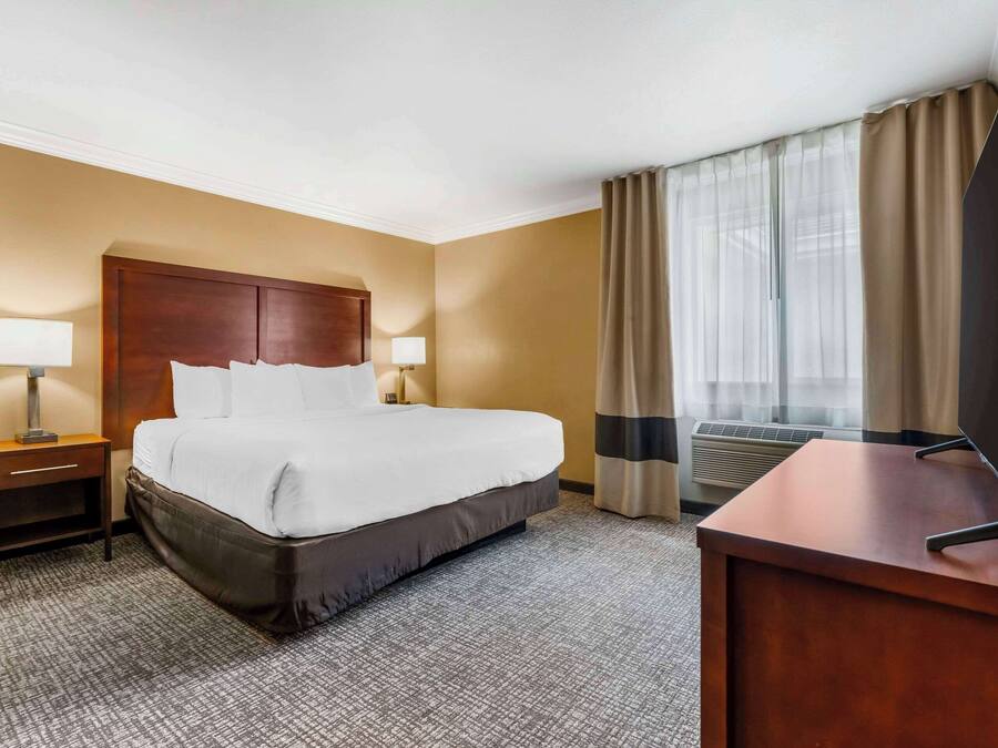 A hotel room with a large bed, two bedside tables with lamps, a desk, and a window with curtains.