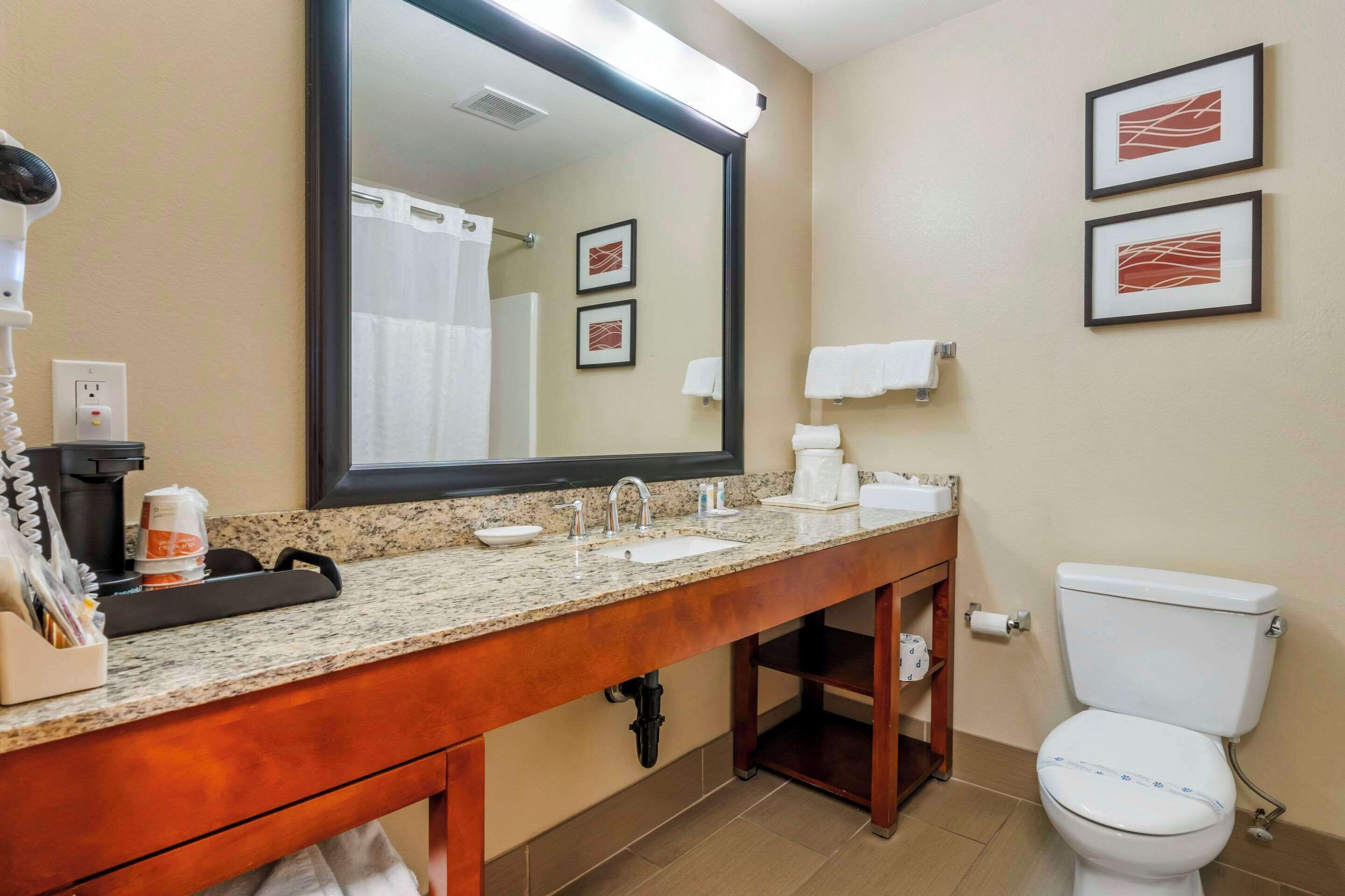 A bathroom with a granite countertop sink, a large mirror, a toilet, and two framed pictures on the wall.