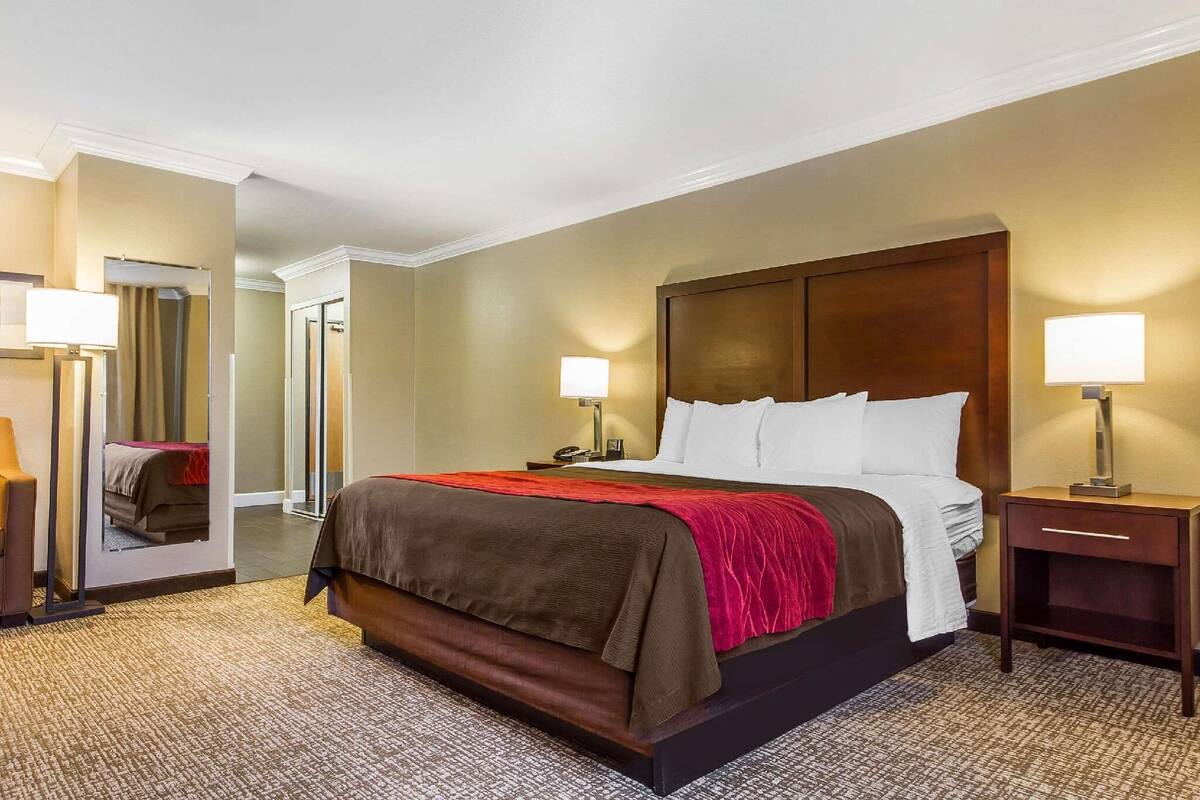 A hotel room with a large bed, bedside lamps, a nightstand, and a mirror.