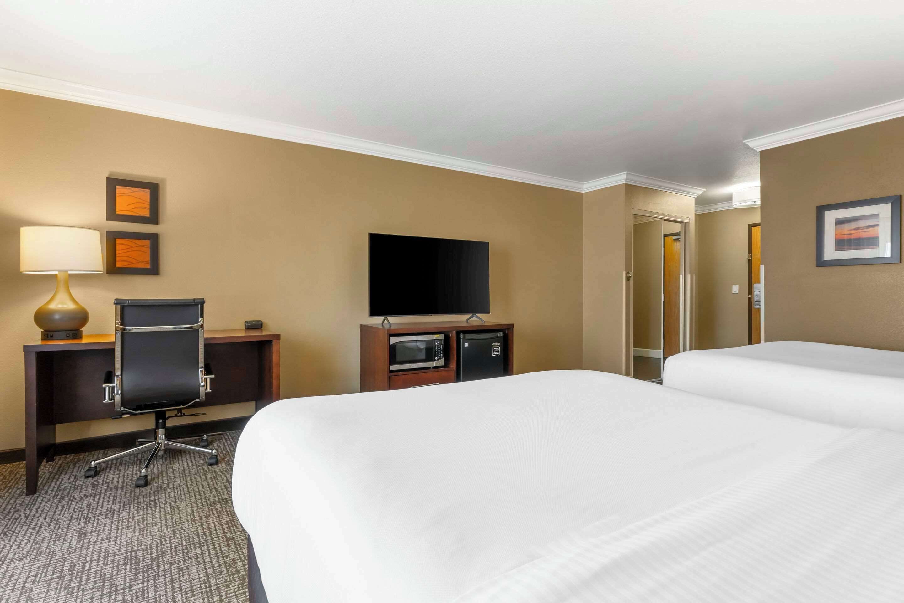 Quarto de hotel com duas camas, uma escrivaninha com cadeira, TV de tela plana, micro-ondas e um pequeno frigorífico.