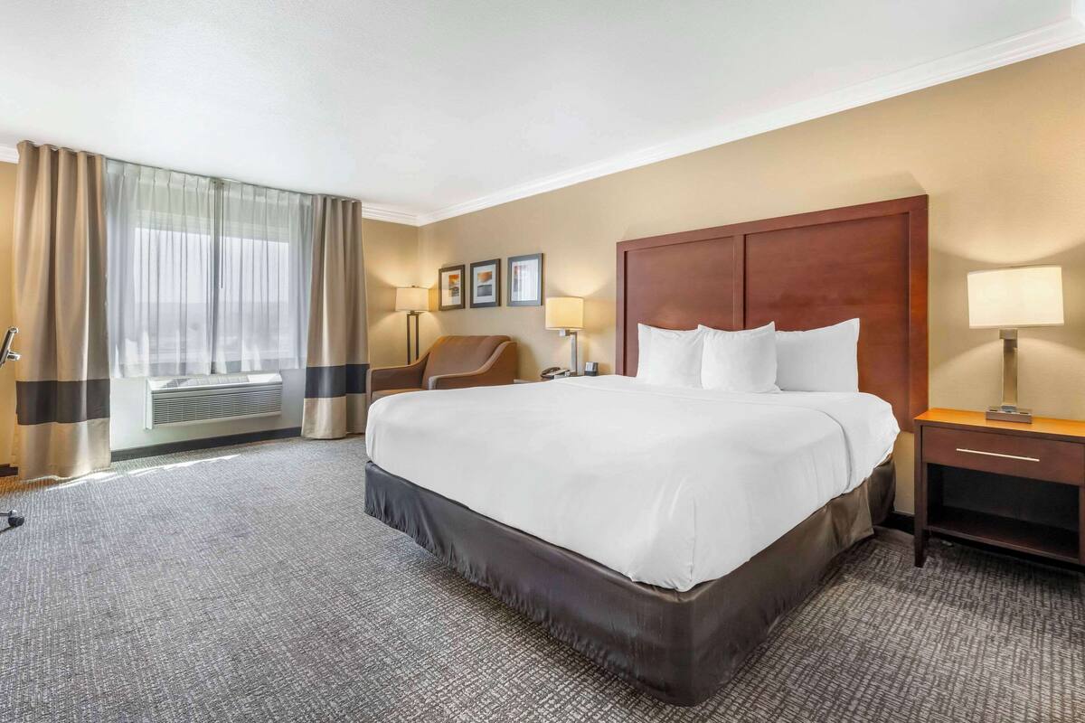 A hotel room with a large bed, a chair, a desk, and a window with curtains.