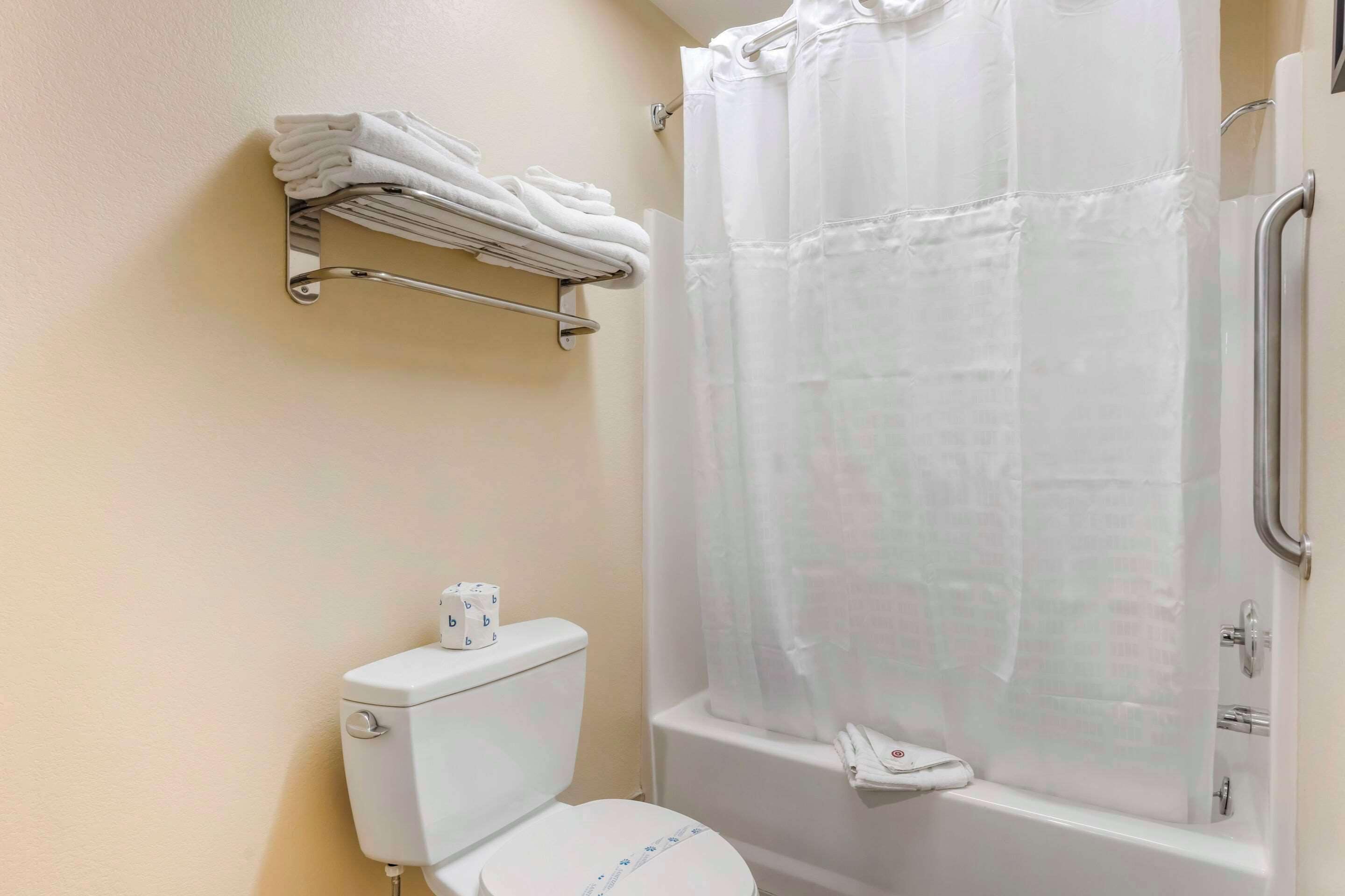 Un baño con inodoro, ducha con cortina y toallero con toallas dobladas.
